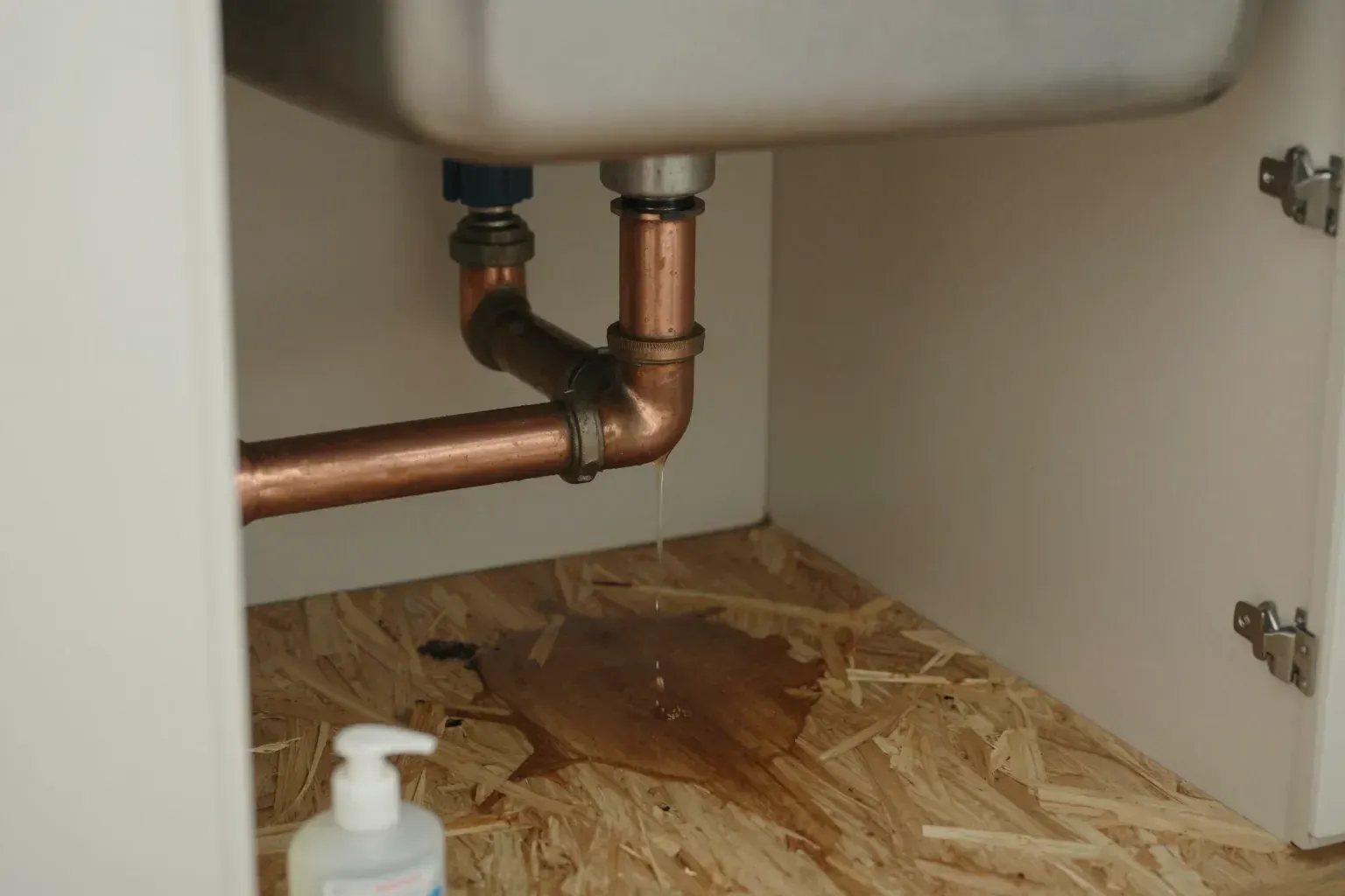 Water dripping from a pipe joint under a kitchen sink onto a wet cabinet floor